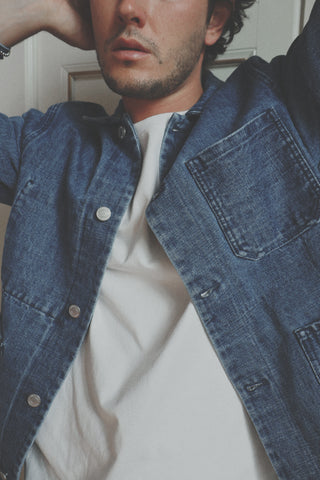 Lifestyle close-up detail of the Barbanera Fallen Cloud blue selvedge denim jacket, highlighting the fabric texture, stitching, and button hardware while worn indoors.